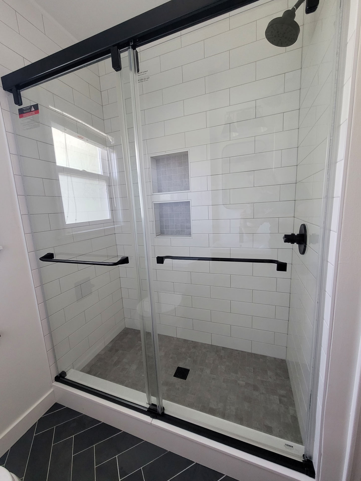 A modern wet space features white subway tile walls, two built-in niches, glass sliding doors with black handles, and a matte black showerhead and controls—ideal for a stylish bath remodel.