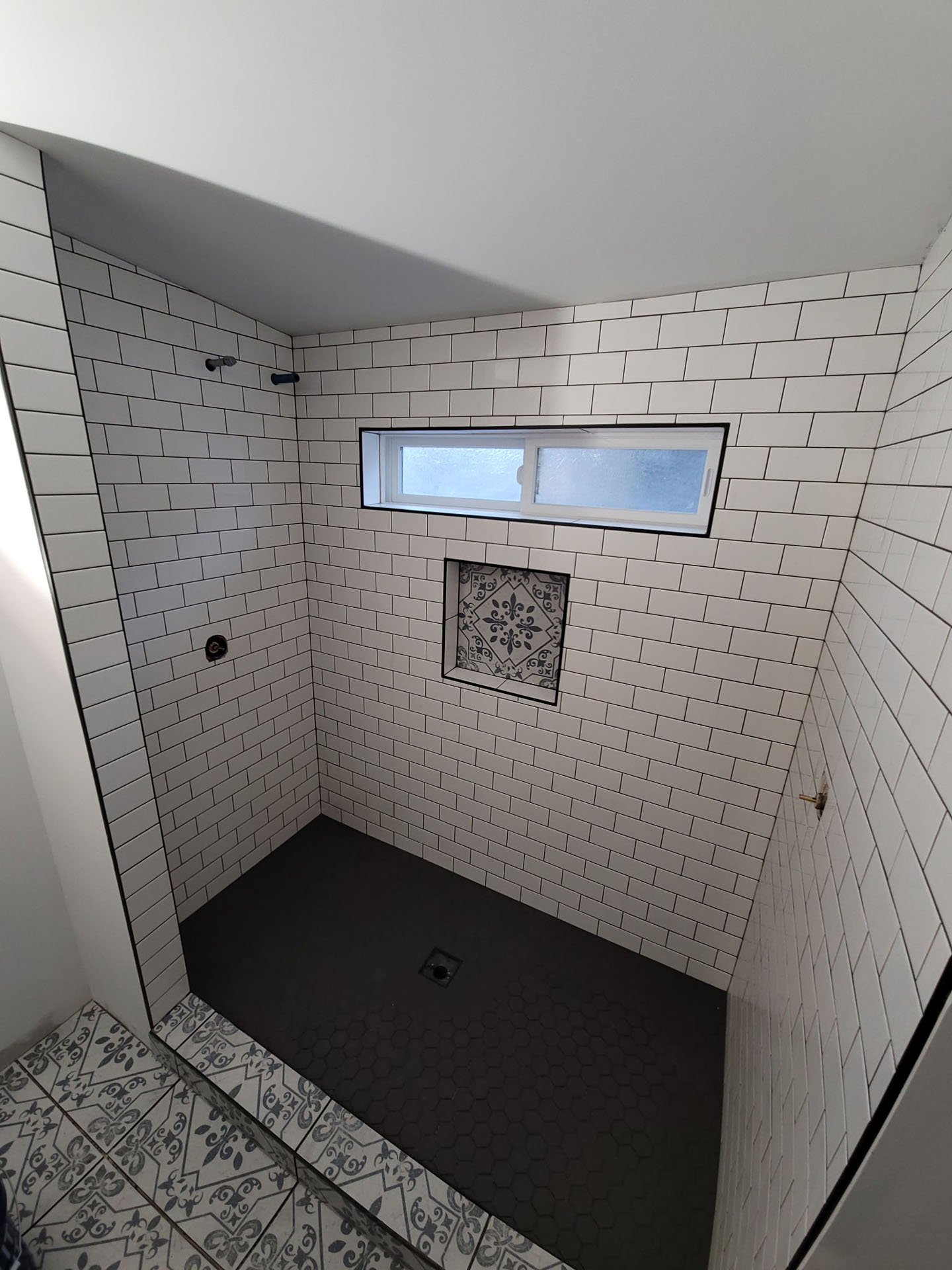 A shower area with white subway tile walls, a black hexagon tile floor, a rectangular window, and a decorative tile niche—perfect inspiration for your bathroom remodel in Phoenix.